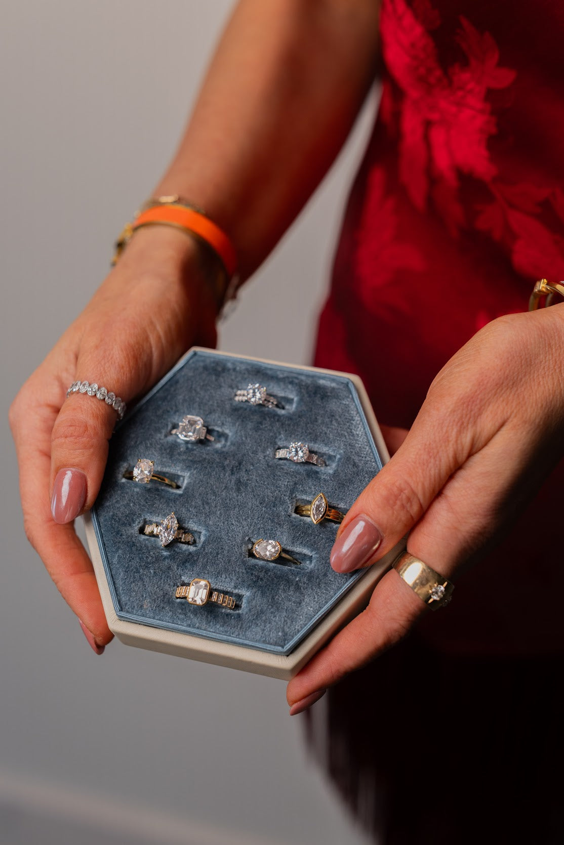 A selection of diamond rings in a blue velvet tray, held by a woman wearing a red dress