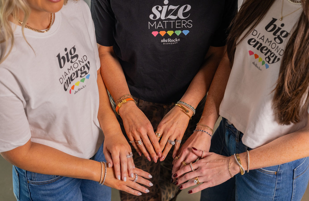 Three women wearing sheRocks Size Matters and Big Diamond Energy shirts, showing their jewelry
